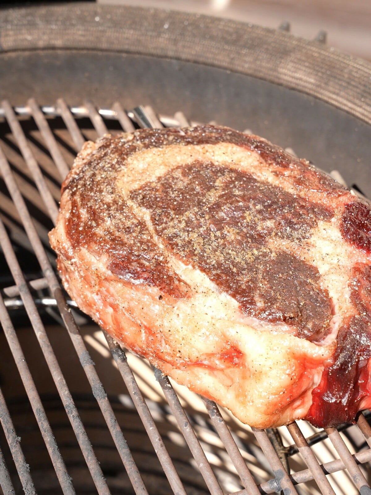 Raw ribeye steak cooking over the indirect zone of the grill.