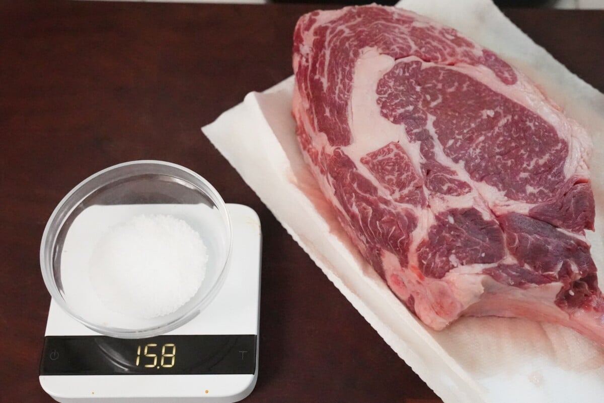 A raw steak next to a scale with salt being weighed in a bowl.