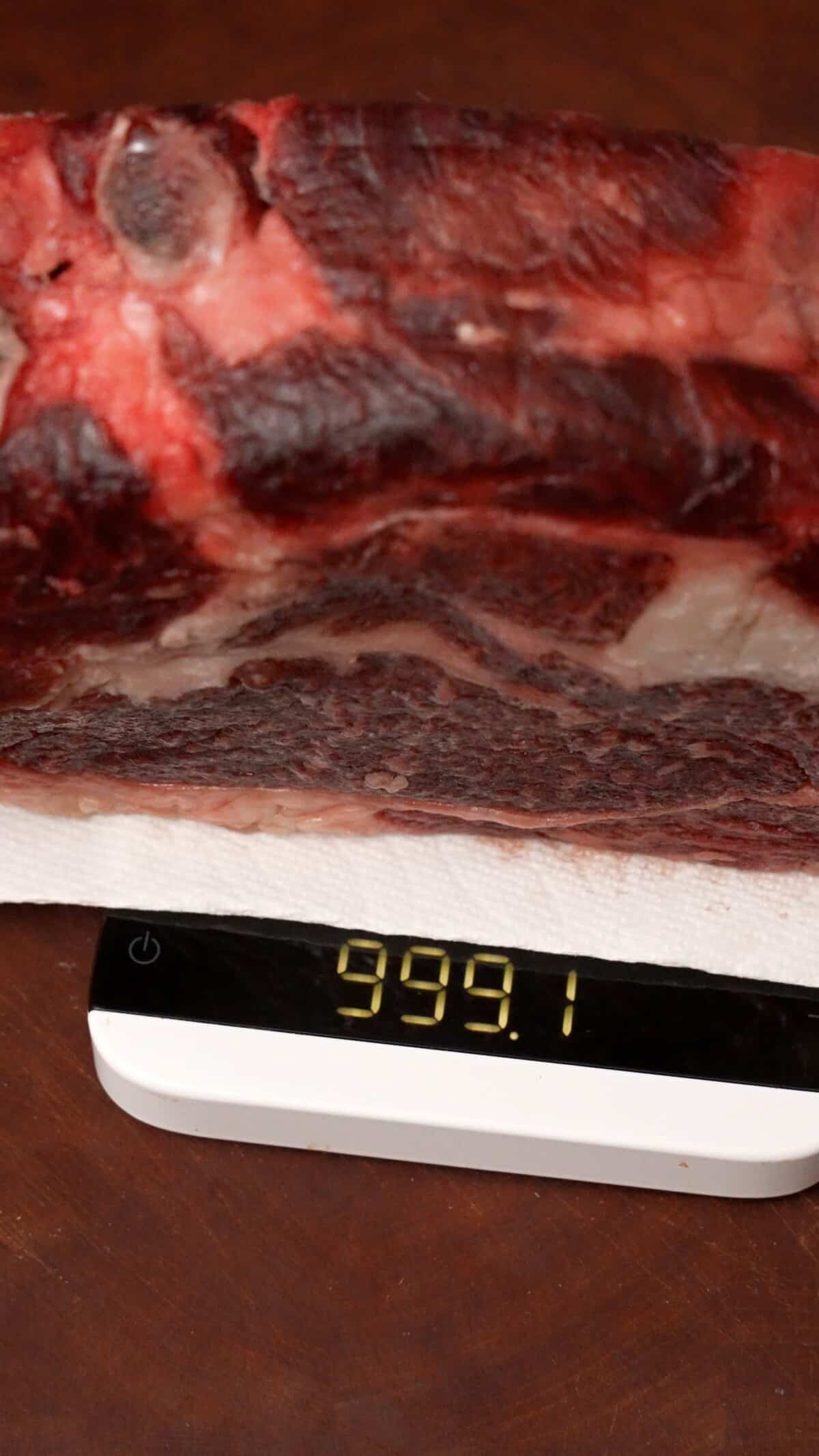 Steak on a scale after dry brining that reads 999 grams.