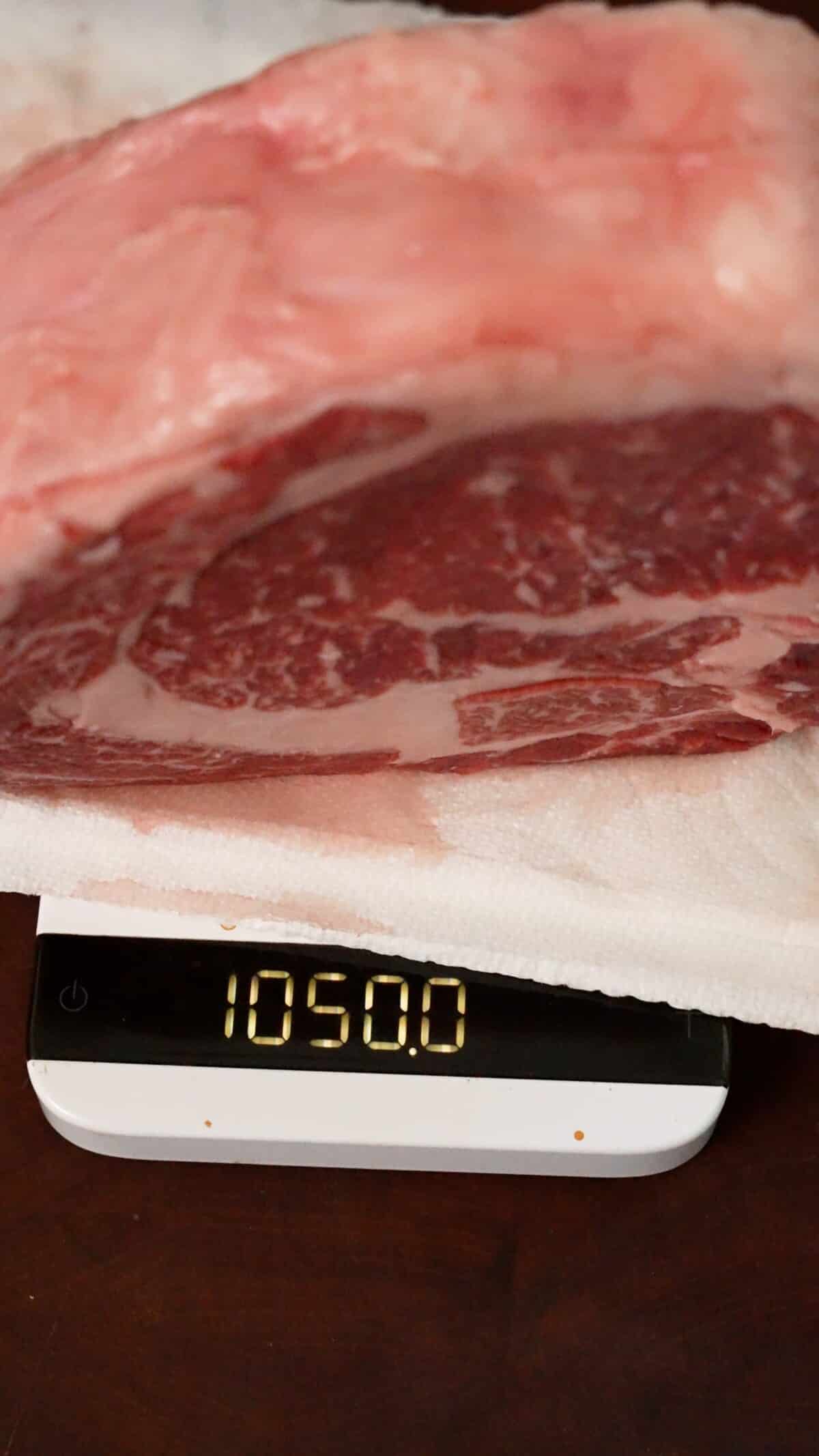 Steak on a scale after dry brining that reads 1050 grams.