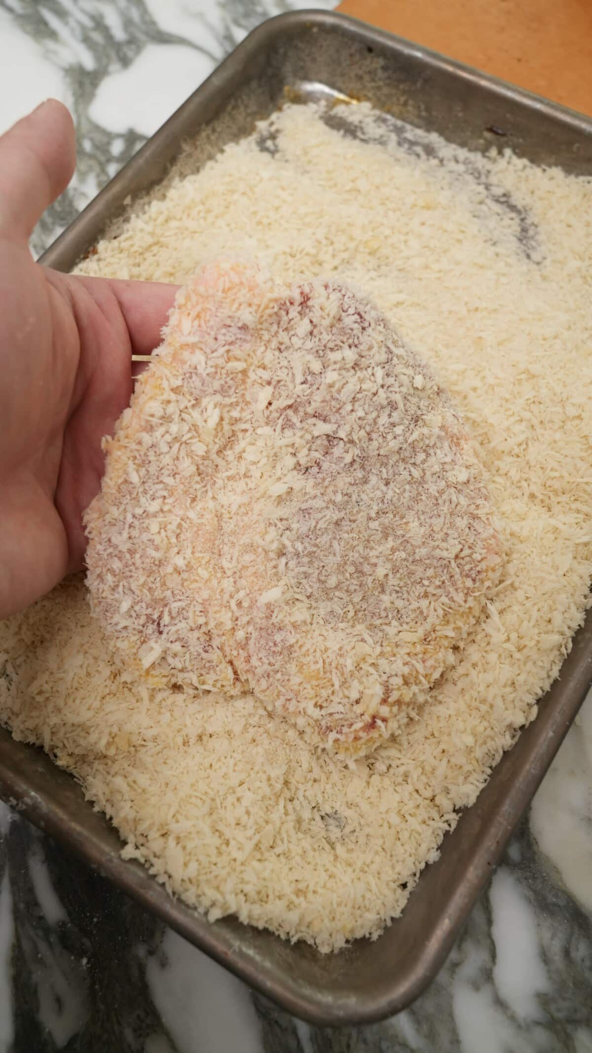 A piece of pork loin being coated in panko breadcrumbs.