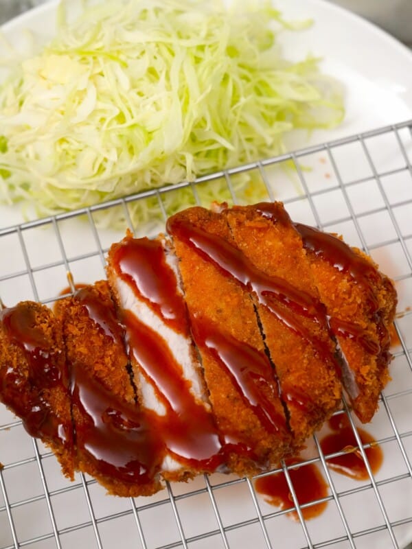 Pork Katsu or Tonkatsu topped with Tonkatsu sauce next to thinly shredded cabbage.