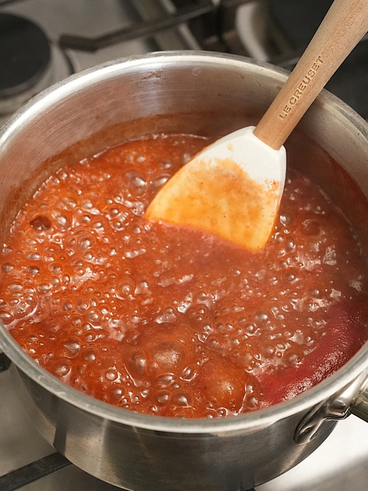 A spatula mixing BBQ sauce in a small saucepan as it boils.