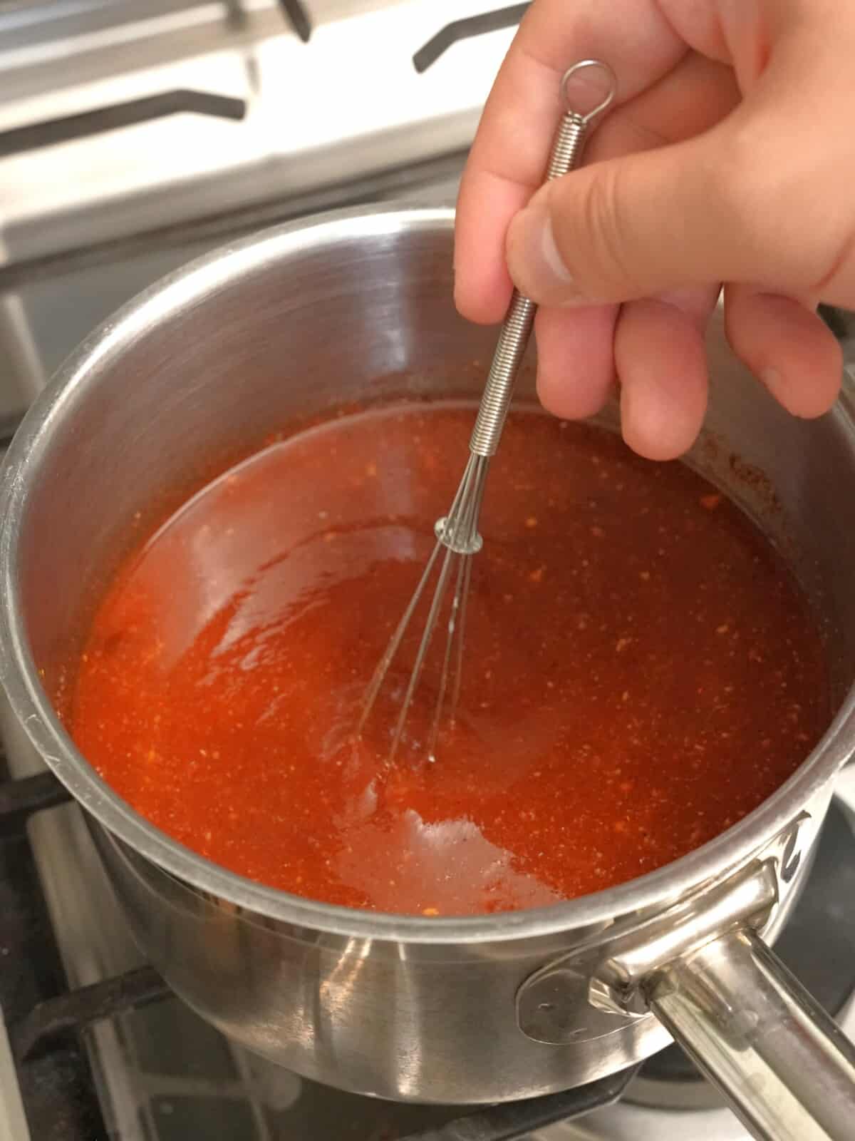 Mixing BBQ sauce in a saucepan with a small whisk.