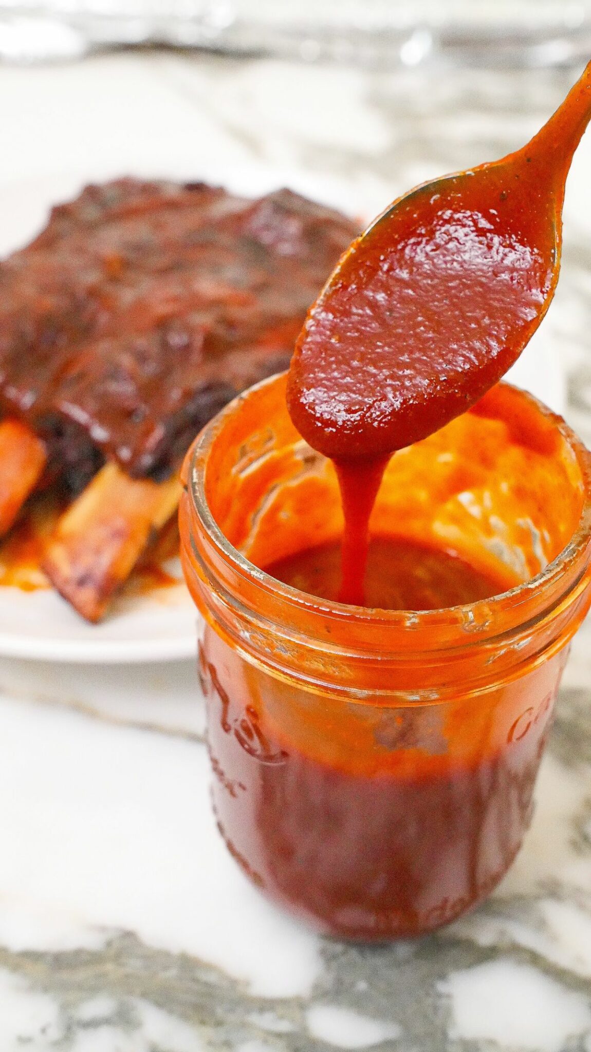 Easy homemade BBQ sauce in a jar next to a rack of ribs.