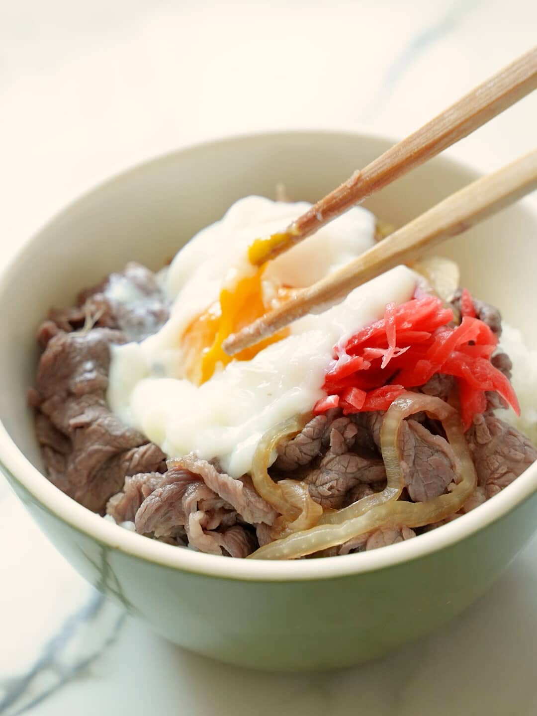 A ramen egg being topped on beef gyudon.
