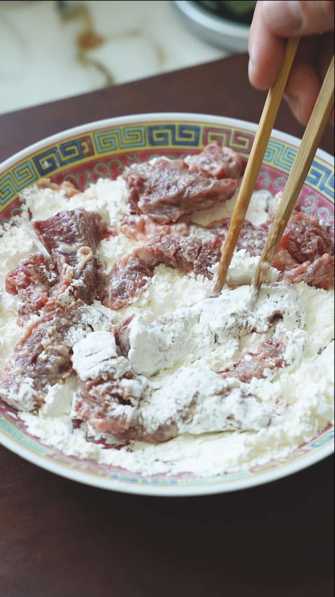 Coating marinated beef in cornstarch.