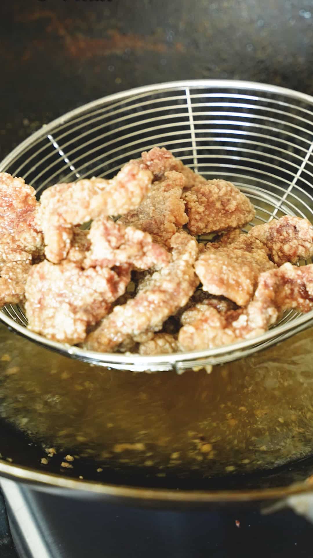 A metal strainer draining freshly fried beef from oil in a wok.