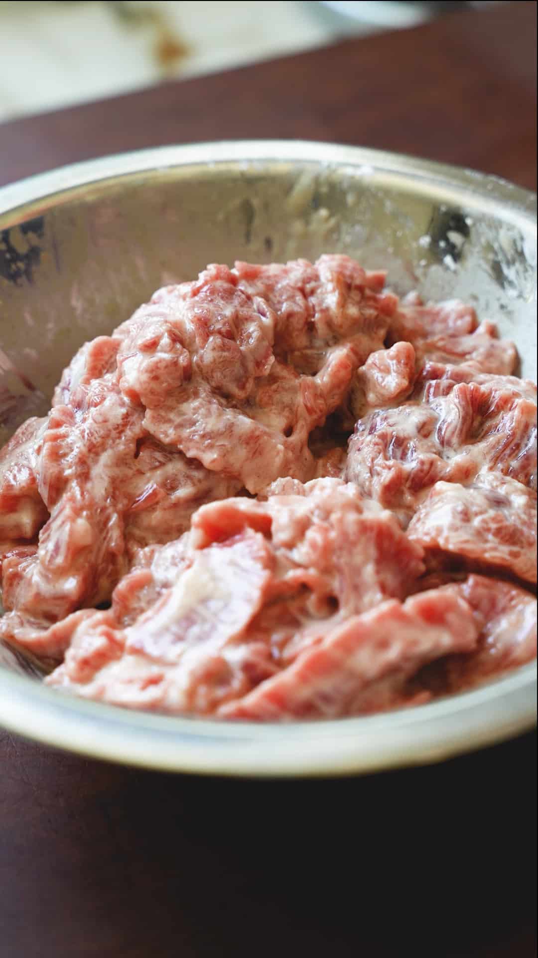 Thinly sliced beef marinated in a cornstarch marinade in a metal bowl.