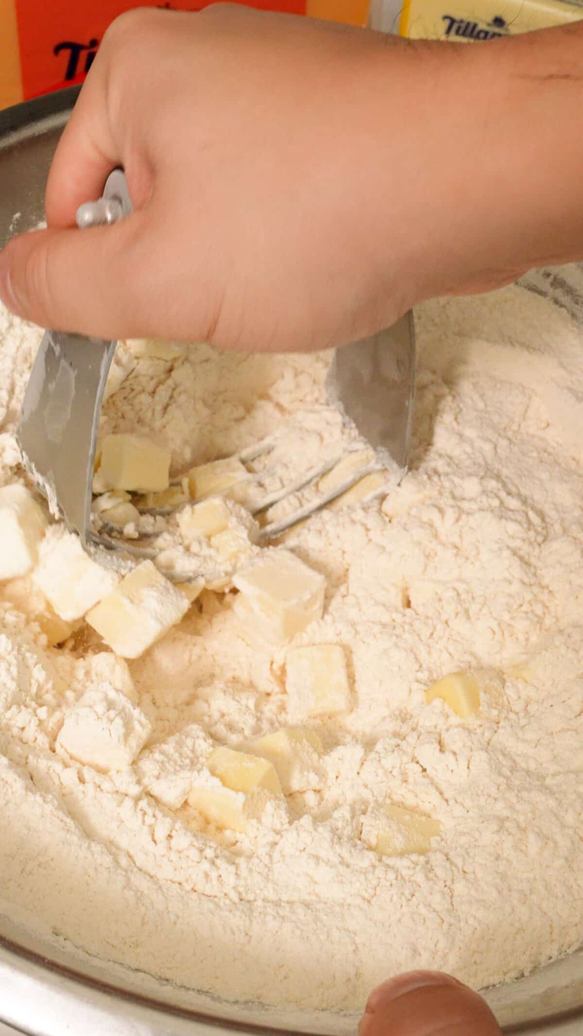 Cubed butter being cut into biscuit dough by a pastry cutter.