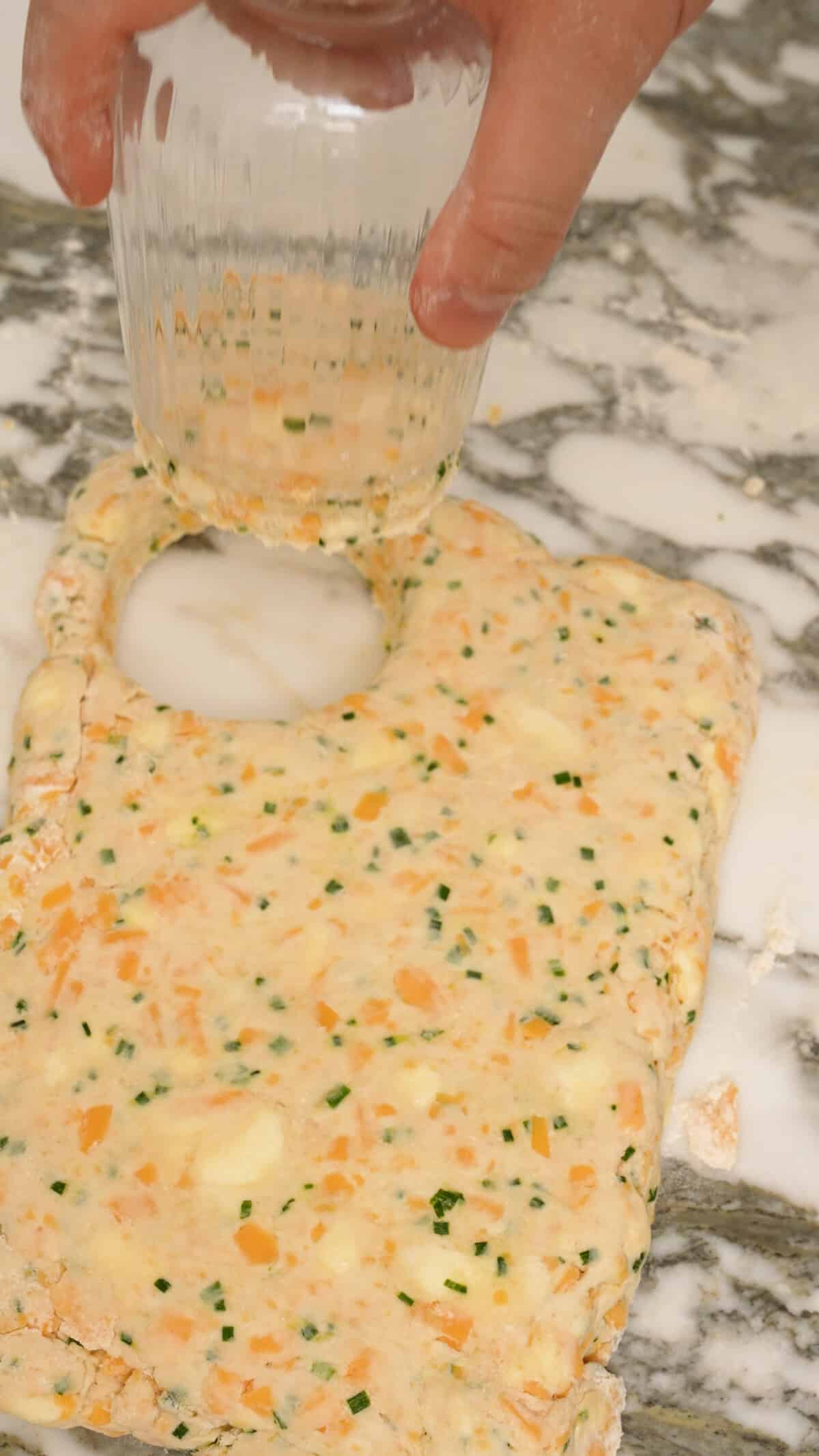 A glass cup cutting the biscuit dough into circles.