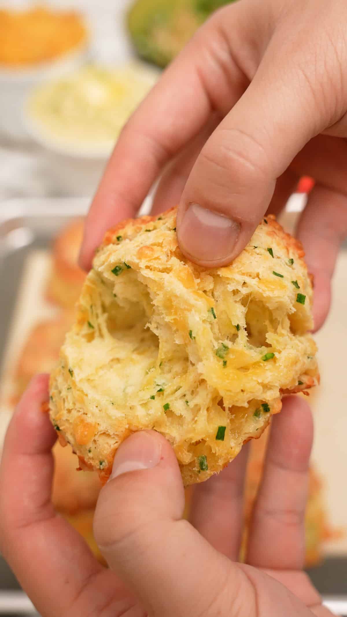 A pair of hands pulling apart a cheddar biscuit showing the flakey layers.