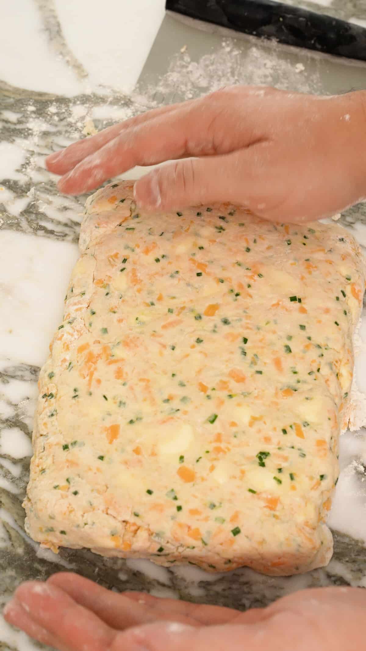 Hands folding the folded biscuit dough into a rectangle.