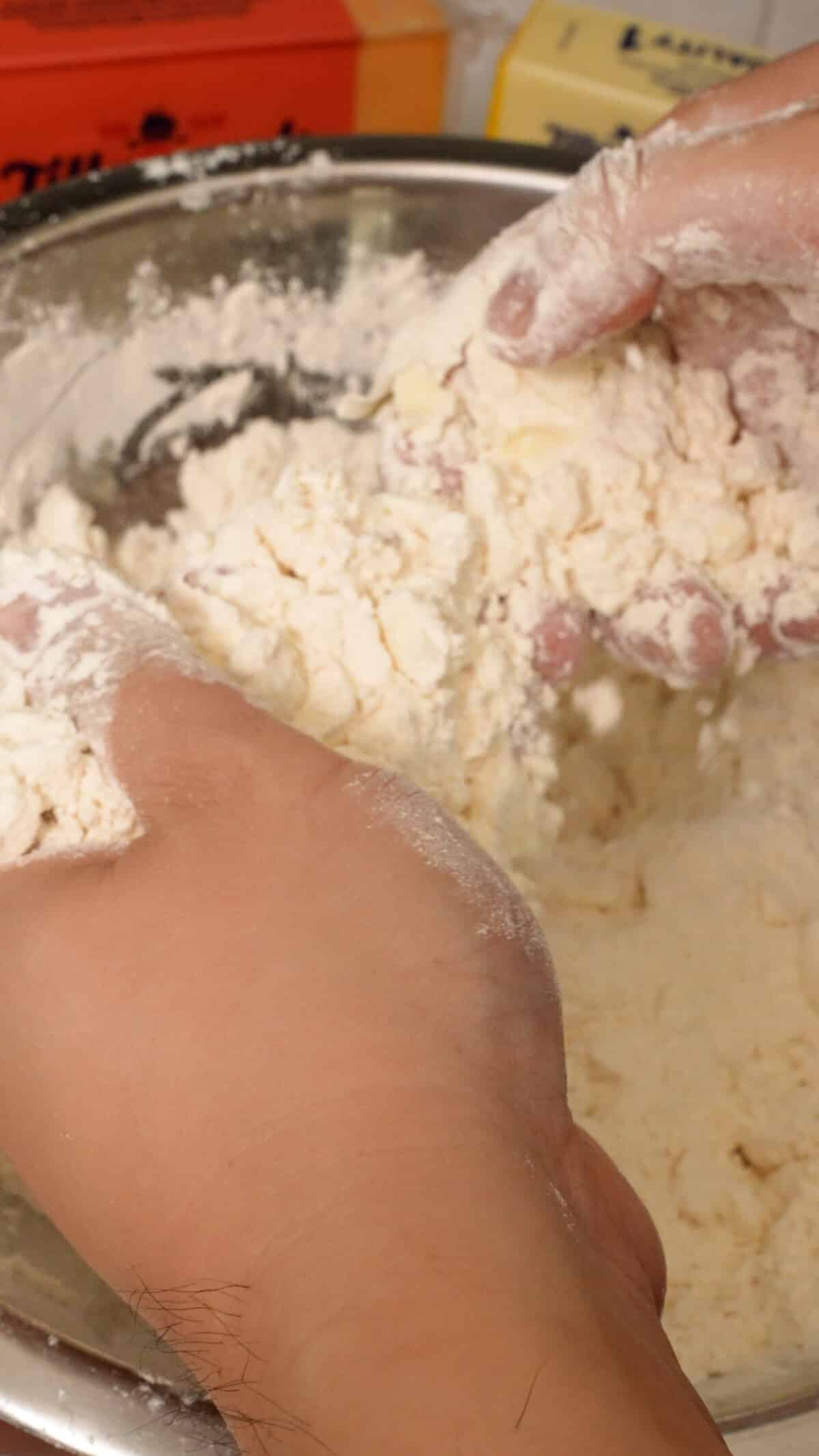 Hands crumbling cold butter into biscuit dough.