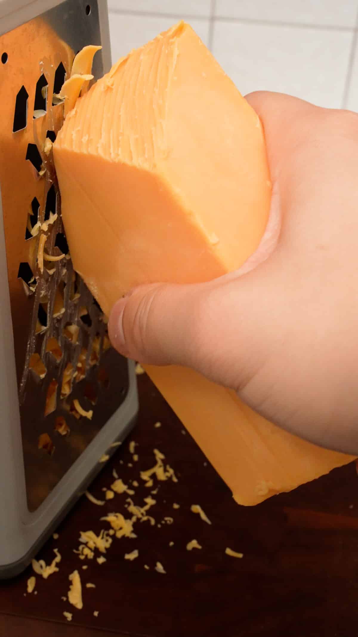 A block of cheddar cheese being shredded on a box grater.