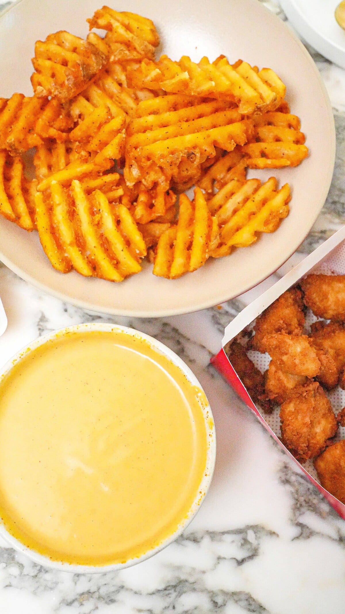 Chick-Fil-A sauce in a bowl with waffle fries and chicken nuggets.