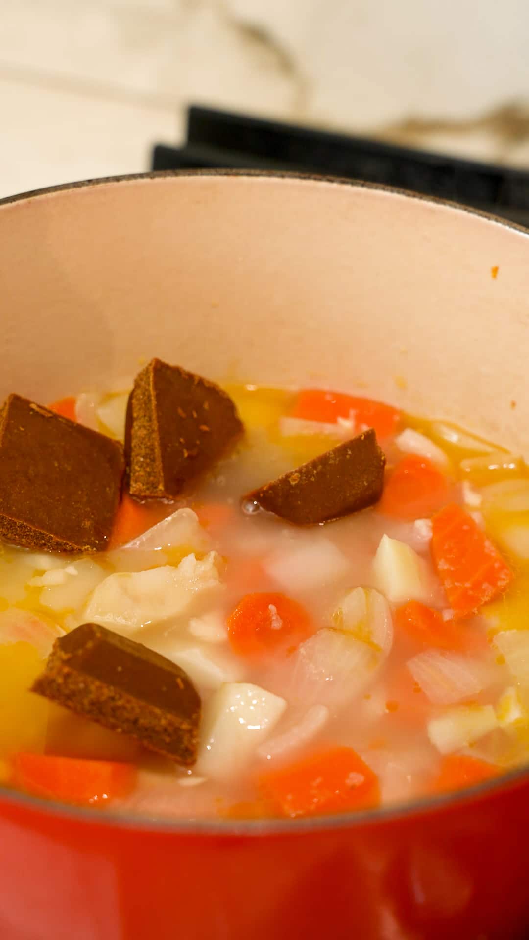 Curry cubes being added to vegetables in a dutch oven.