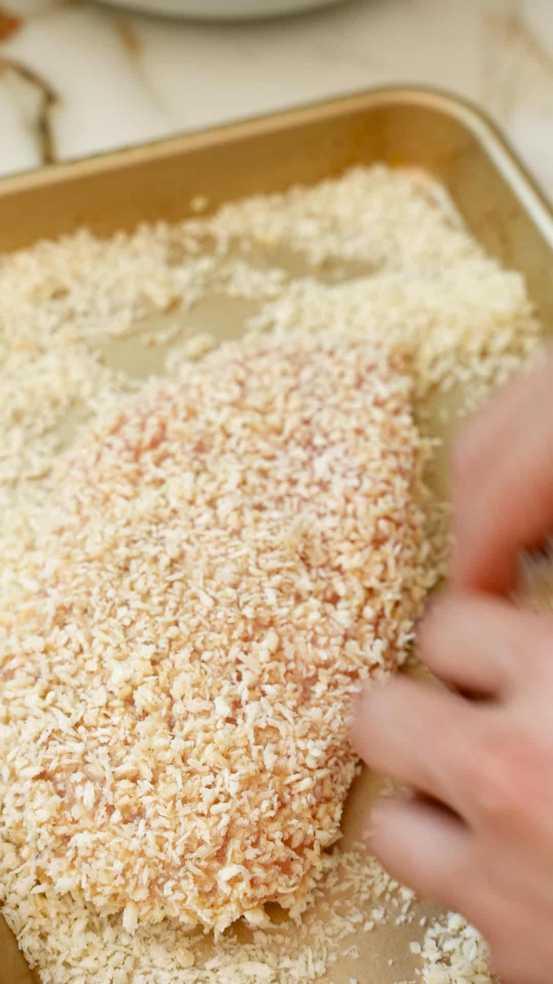 Chicken being breaded with panko breadcrumbs on a tray.