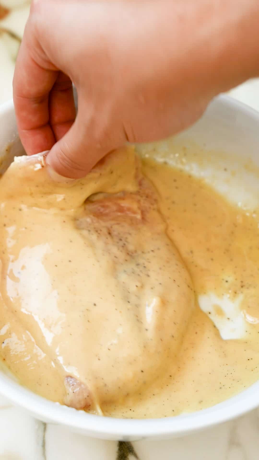 Chicken cutlet being dipped in the wet batter.