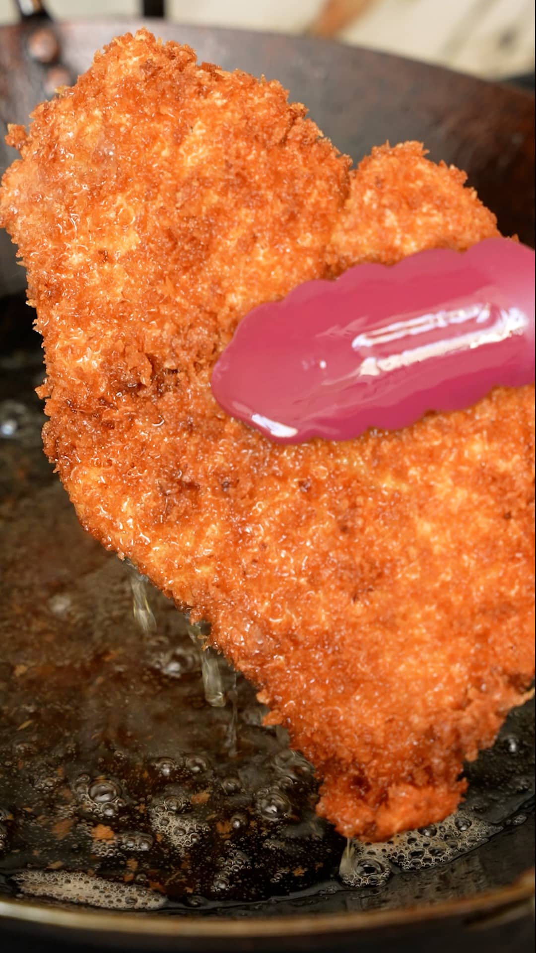 Chicken katsu cutlet being removed from the oil with tongs.