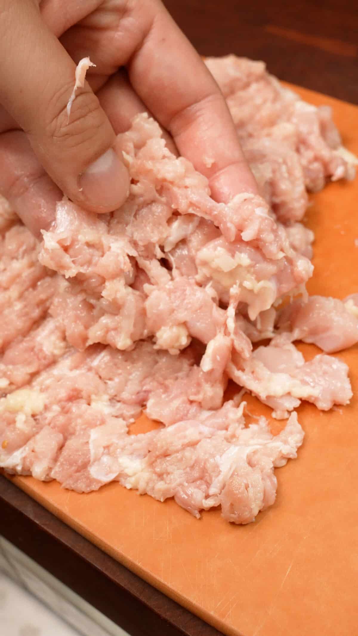 A hand showing texture of the minced chicken thigh on a cutting board.