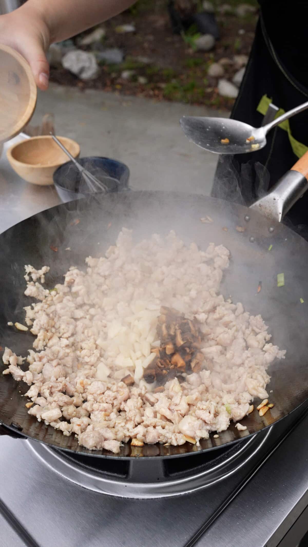 Chopped water chestnuts and mushrooms being added to the chicken in a wok.