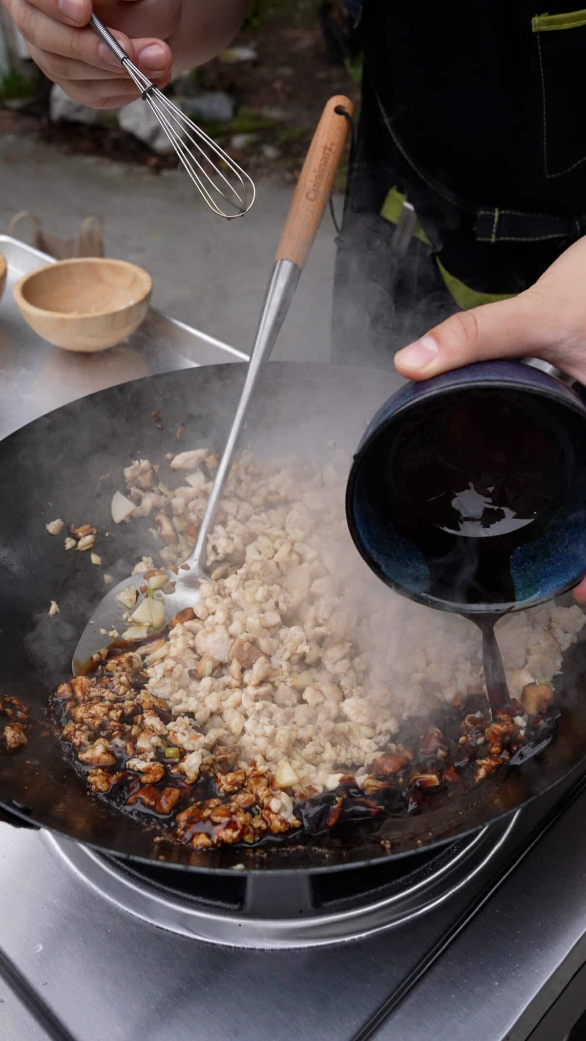 The chicken lettuce wrap sauce being added to the chicken, mushrooms, and water chestnuts in a wok.