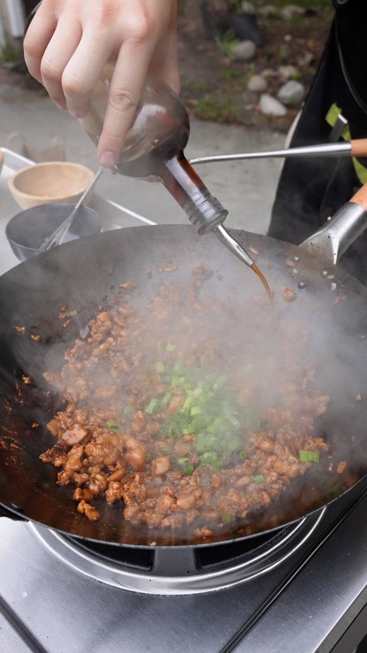 Sesame oil and scallion greens being added to the chicken filling in a wok.