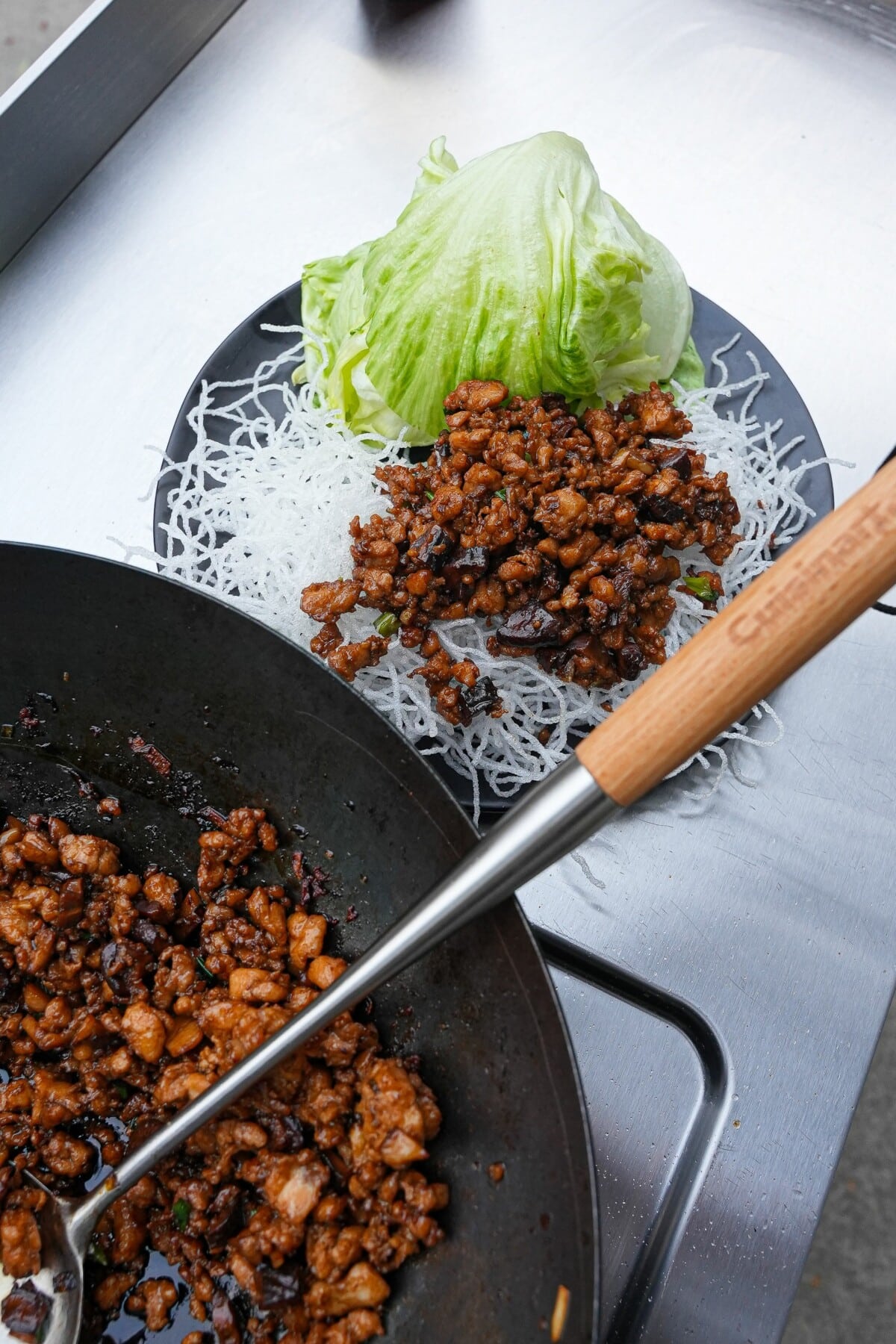 A plate of chicken lettuce wraps next to a wok filled with cooked chicken filling.