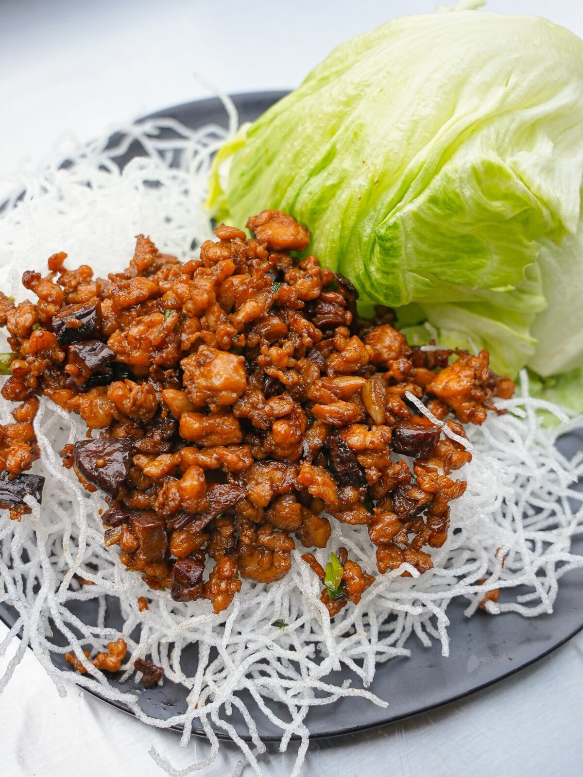 Chicken Lettuce Wraps on a black plate with fried rice vermicelli noodles and green leaf lettuce.