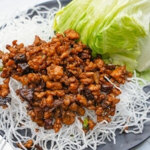 Chicken Lettuce Wraps on a black plate with fried rice vermicelli noodles and green leaf lettuce.