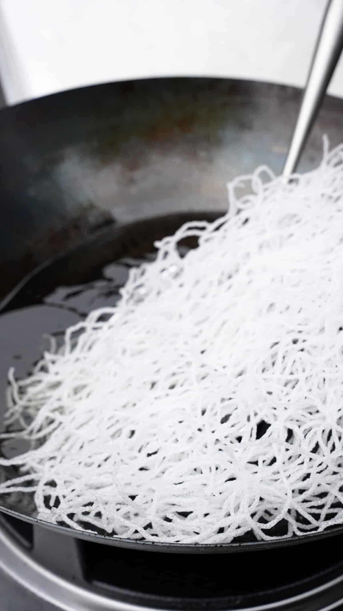 Fried vermicelli rice noodles being puffed up and removed from a wok.