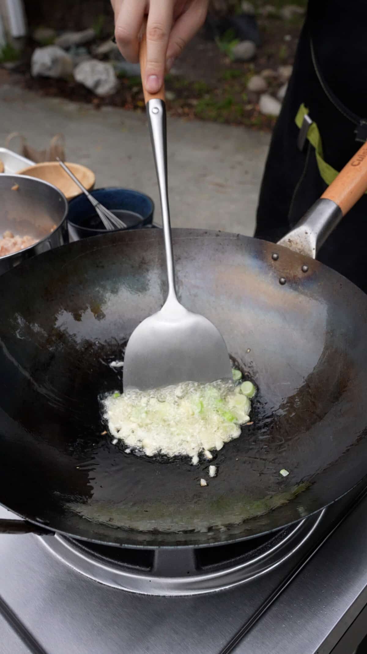 Garlic and scallions being stir fried in a wok with a spatula.