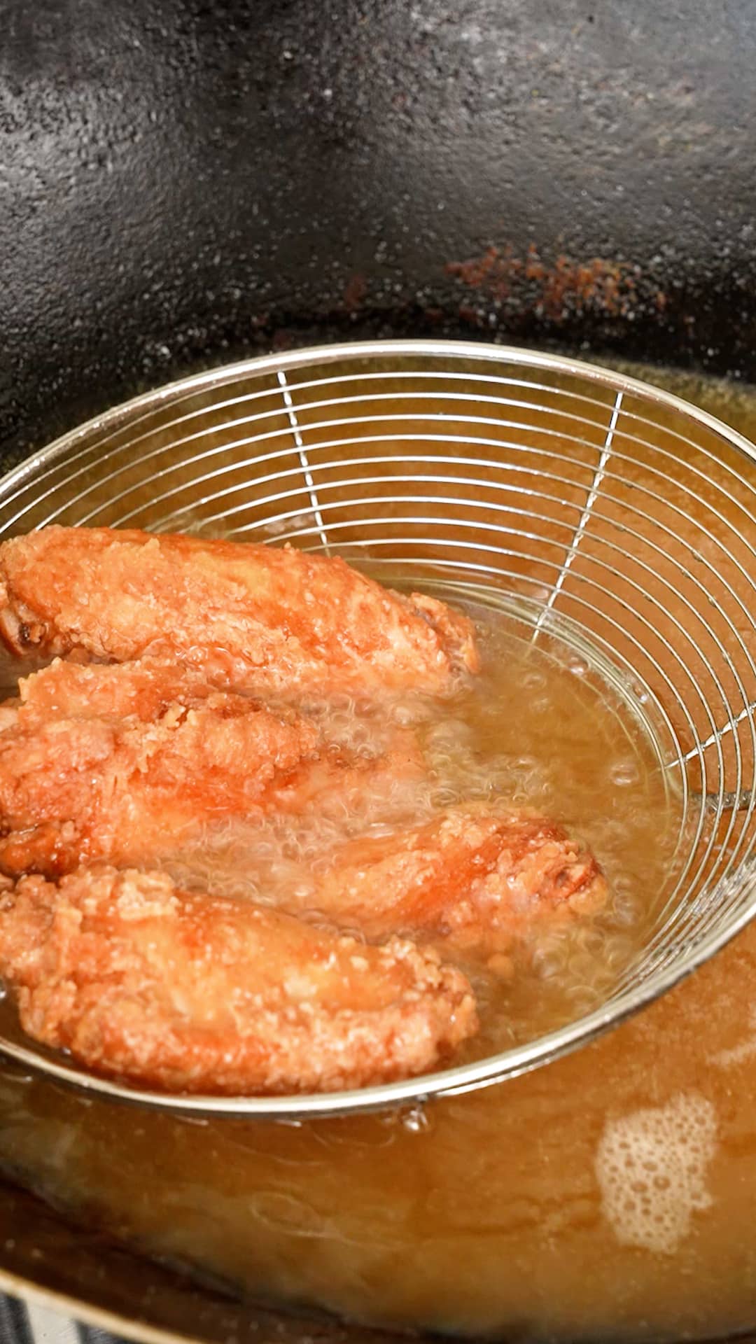 Fried chicken wings being removed from hot oil.