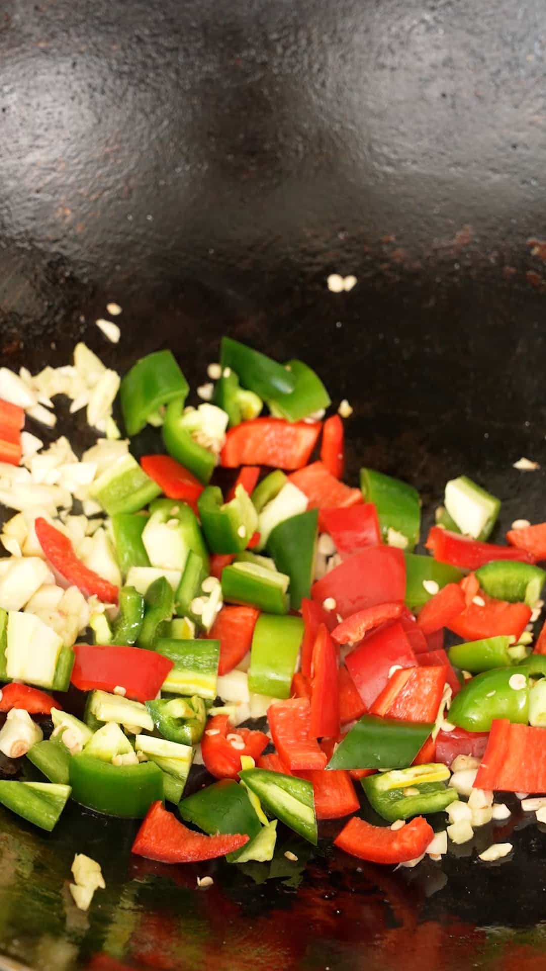 Peppers and garlic being stir fried in a wok.