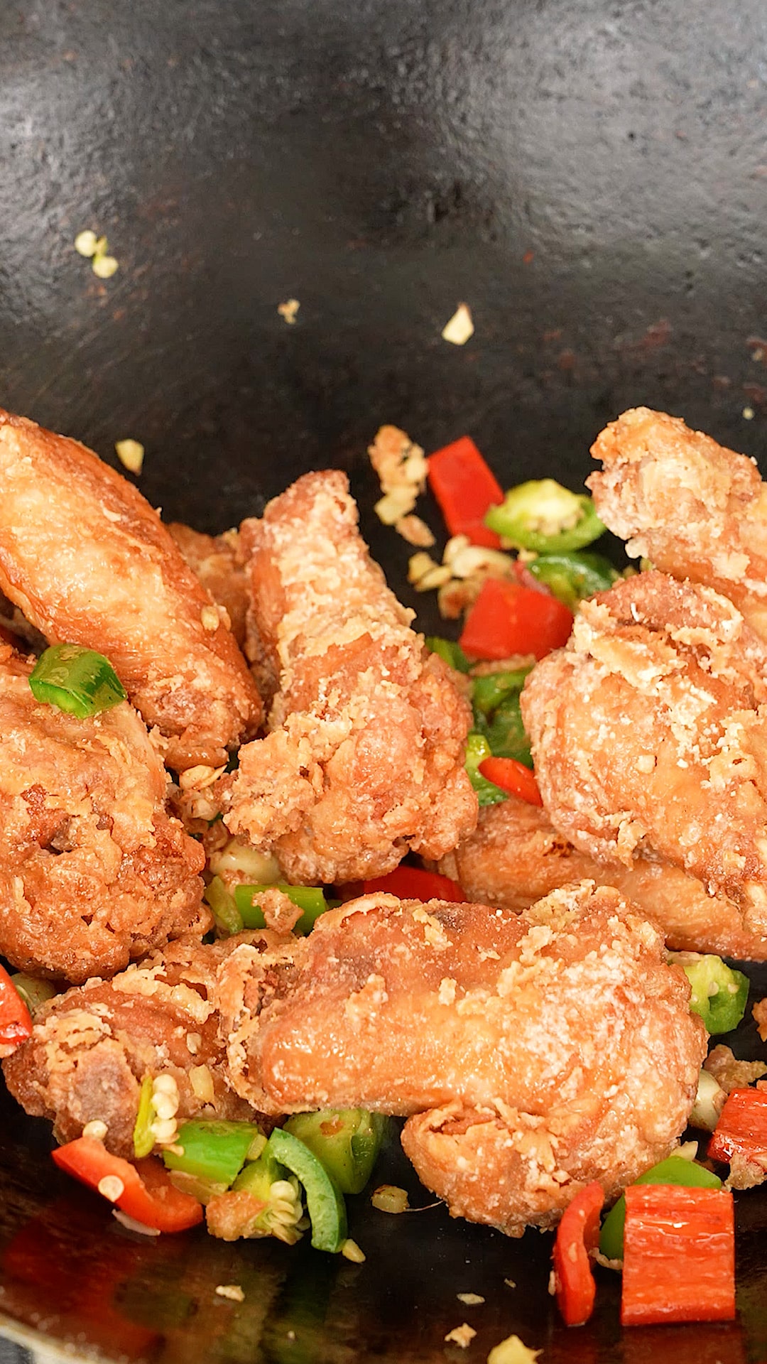 Chicken wings being mixed with peppers in a wok.