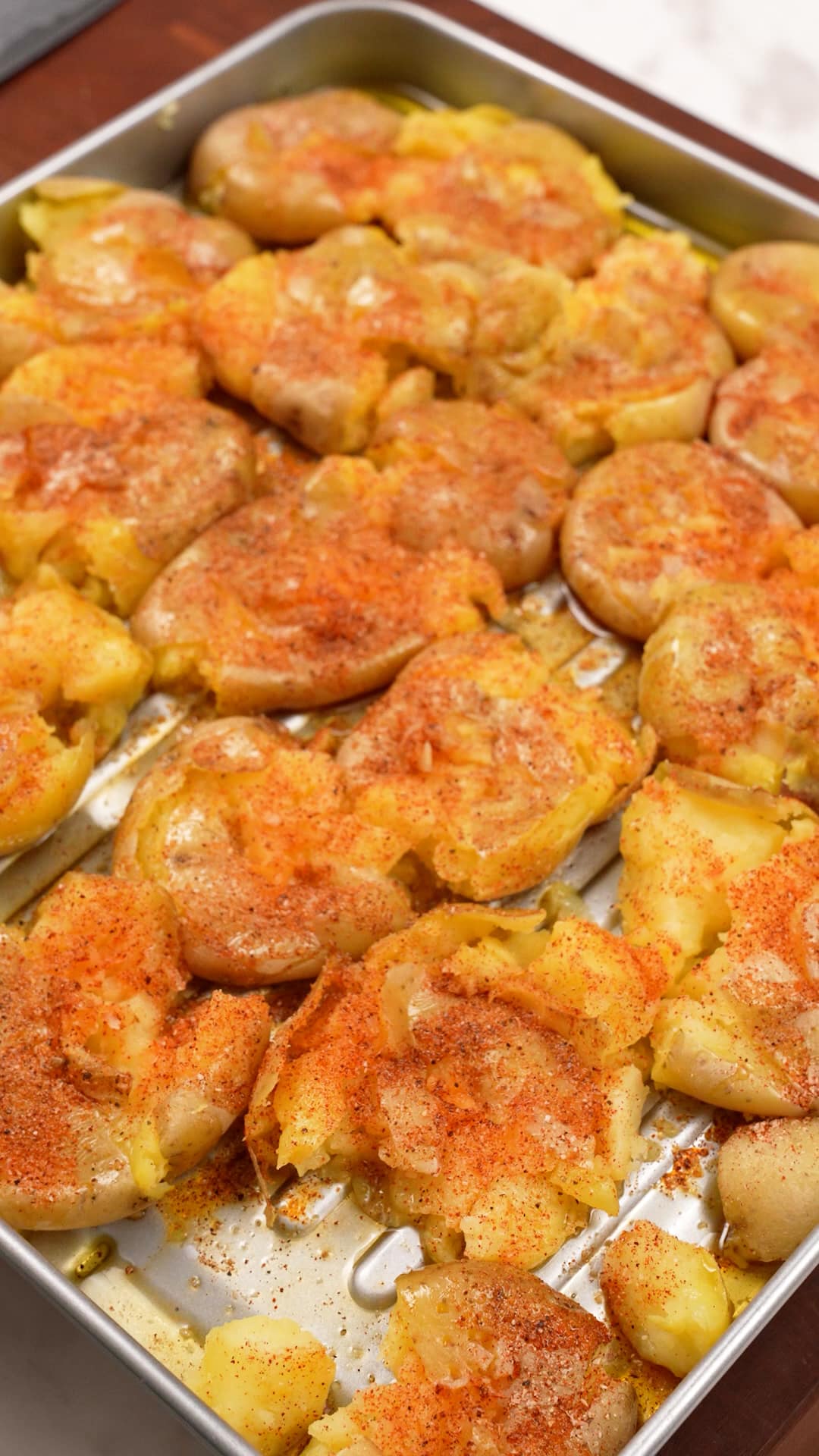 A tray of smashed potatoes seasoned before roasting.