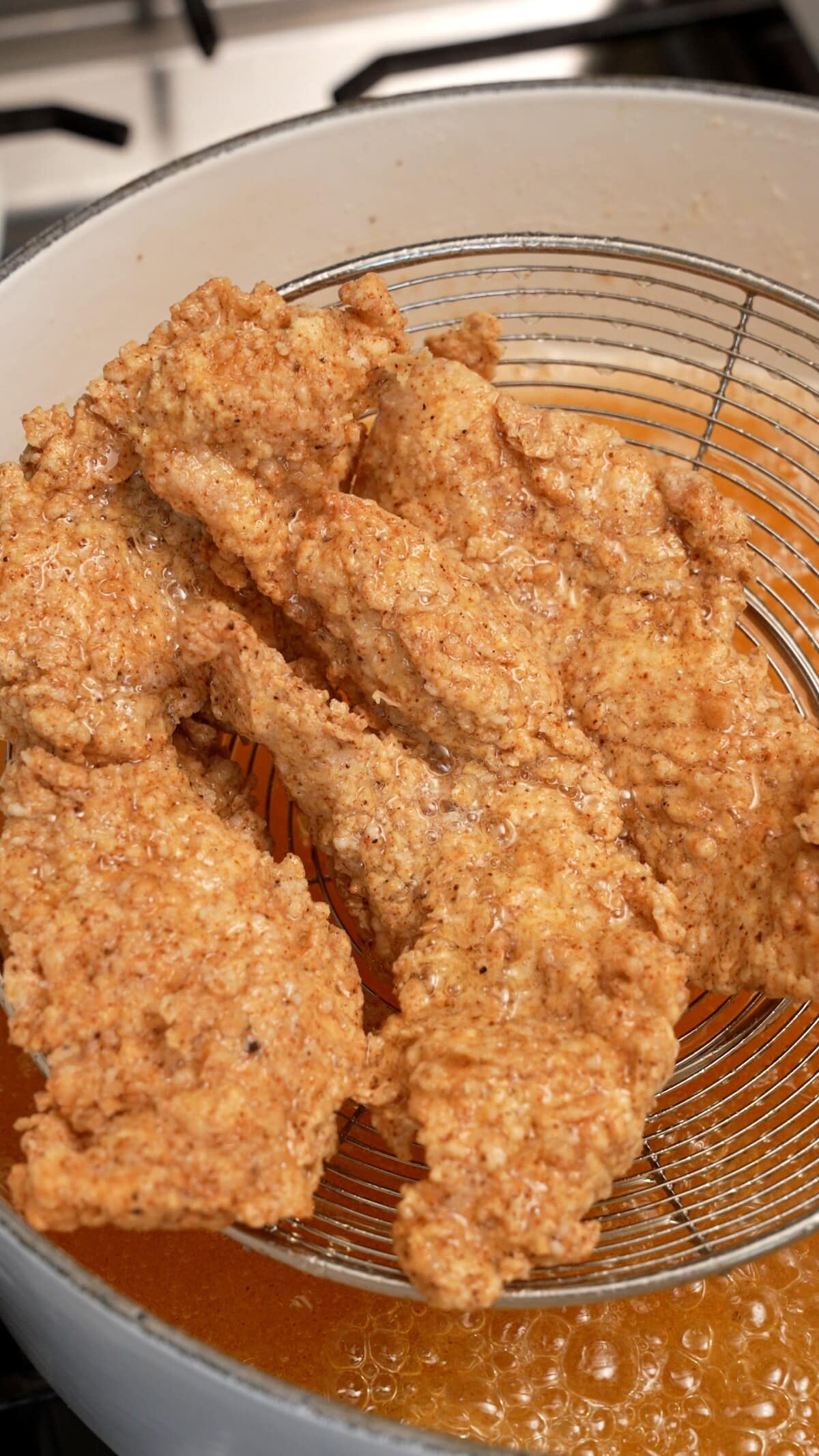 Chicken being strained out of oil from a strainer after being fried.