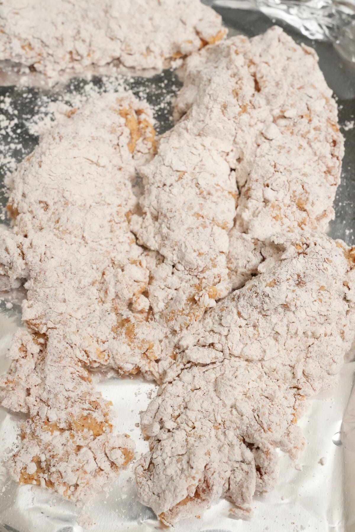 Chicken tenders dredged in dry batter resting on a tray.