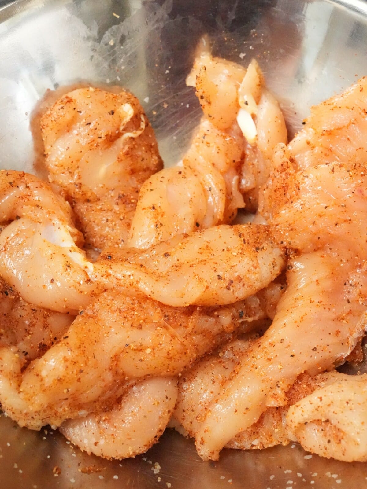 Chicken tenders seasoned in a metal bowl.