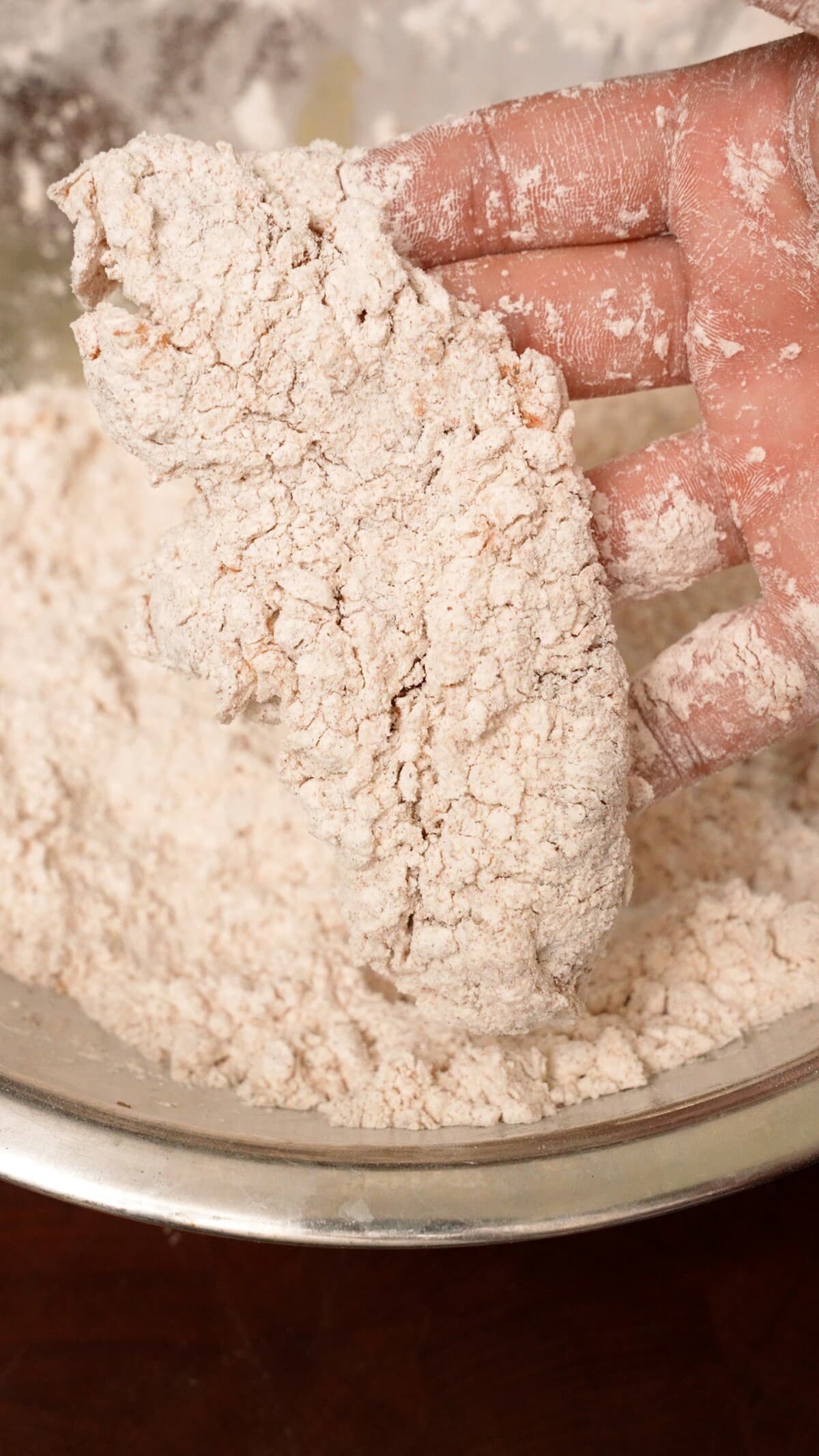 A hand showing a breaded chicken tender over a bowl of dry mix.