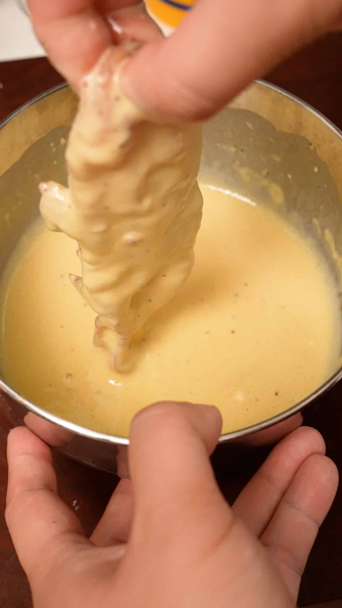 A chicken tender being dredged in the wet batter