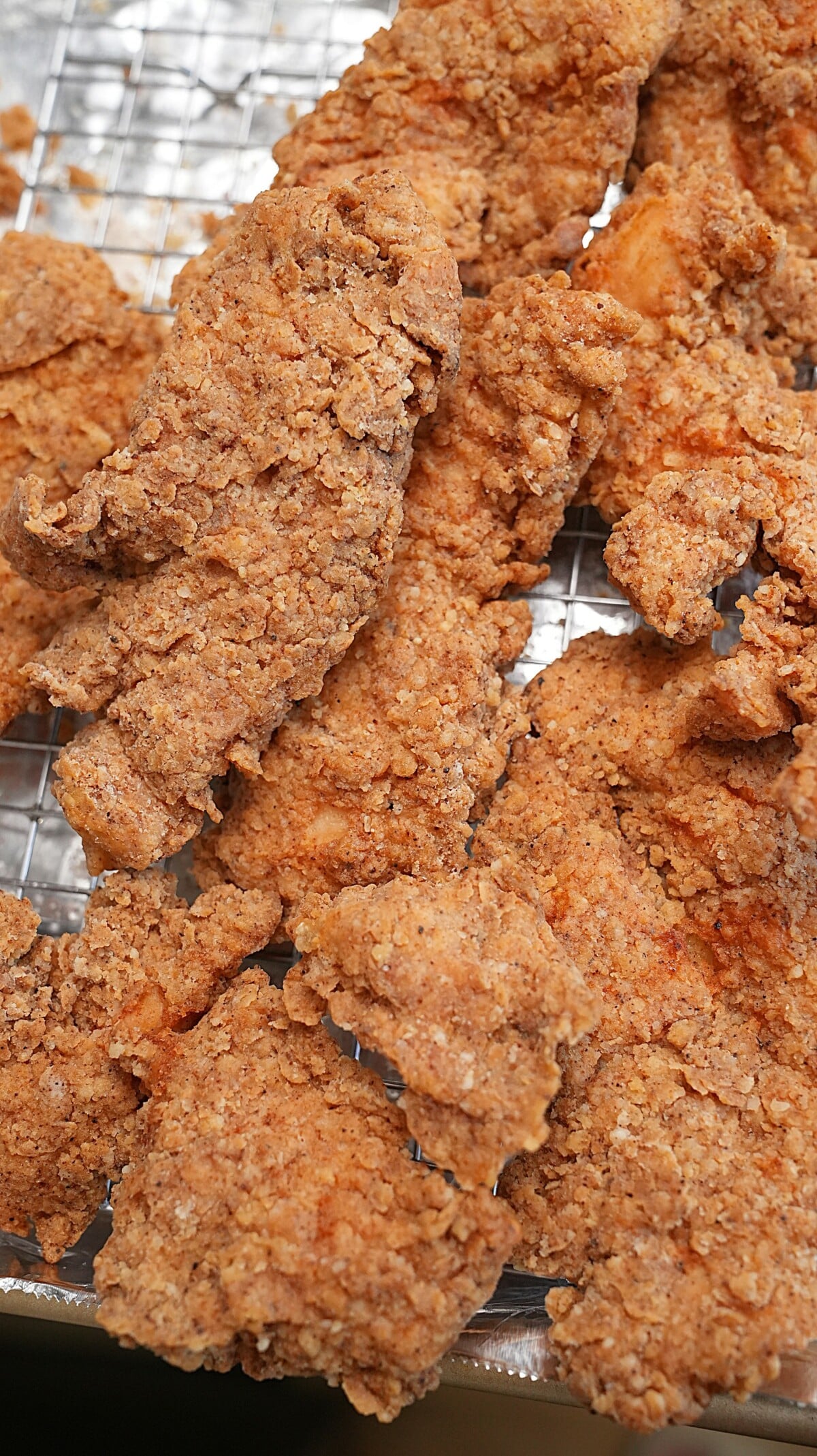 Fried chicken tenders resting on a wire rack after frying.