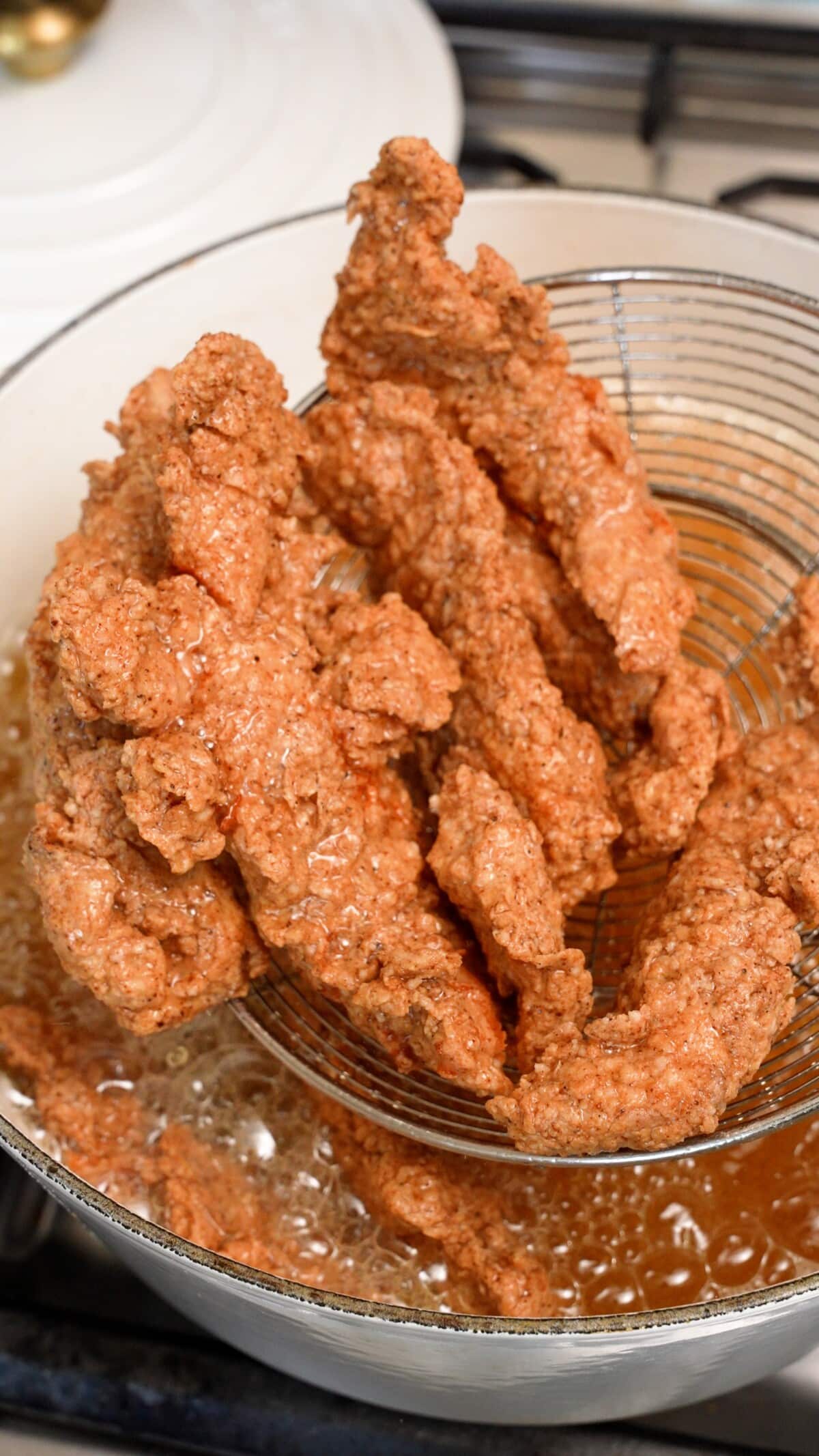 A metal strainer pulling fried chicken tenders out of the oil.