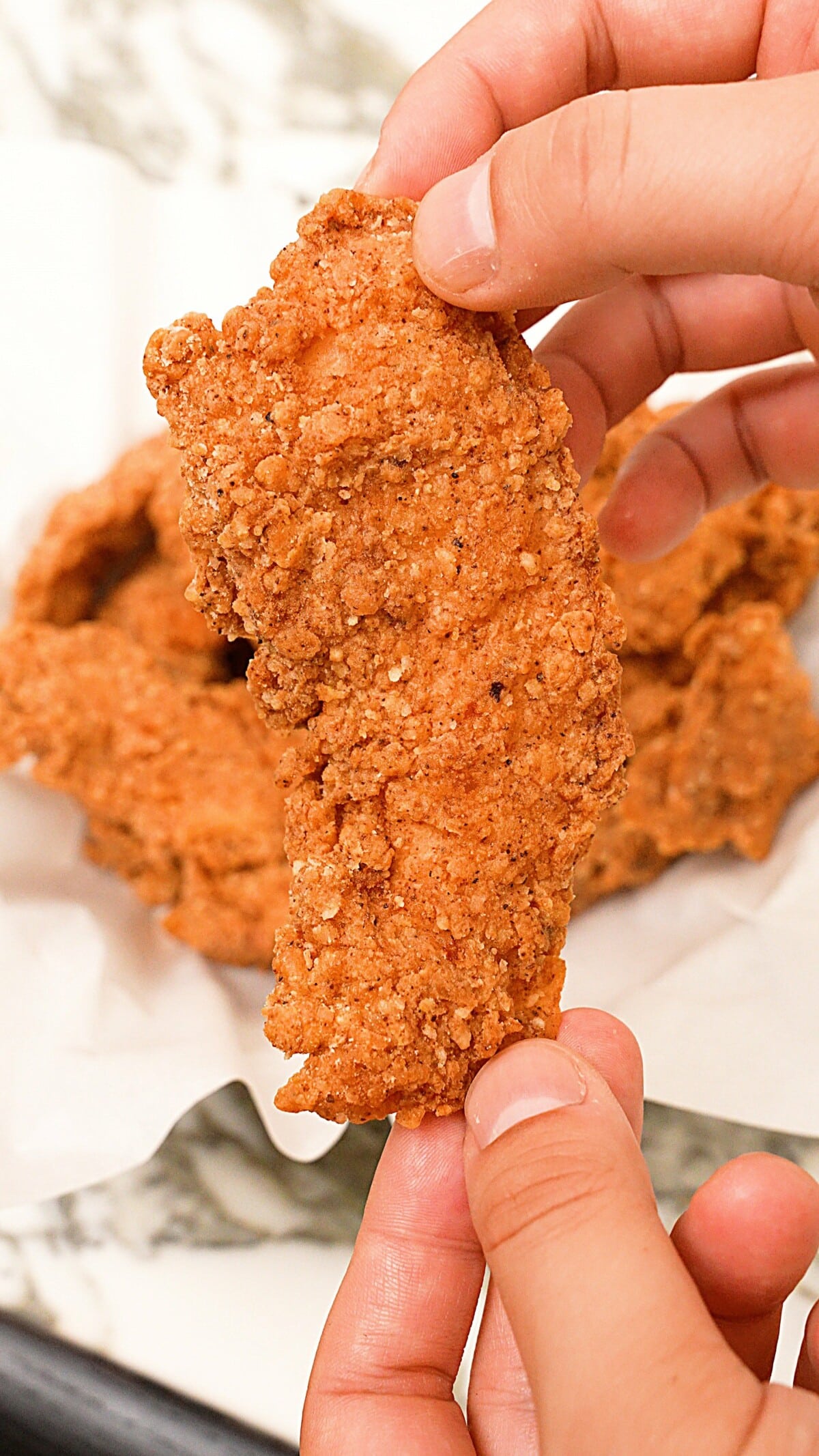 A hand holding up a perfectly fried chicken tender.