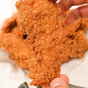 A hand holding up a perfectly fried chicken tender.