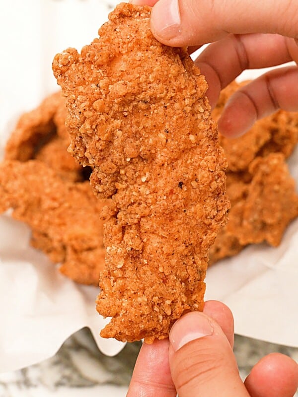 A hand holding up a perfectly fried chicken tender.