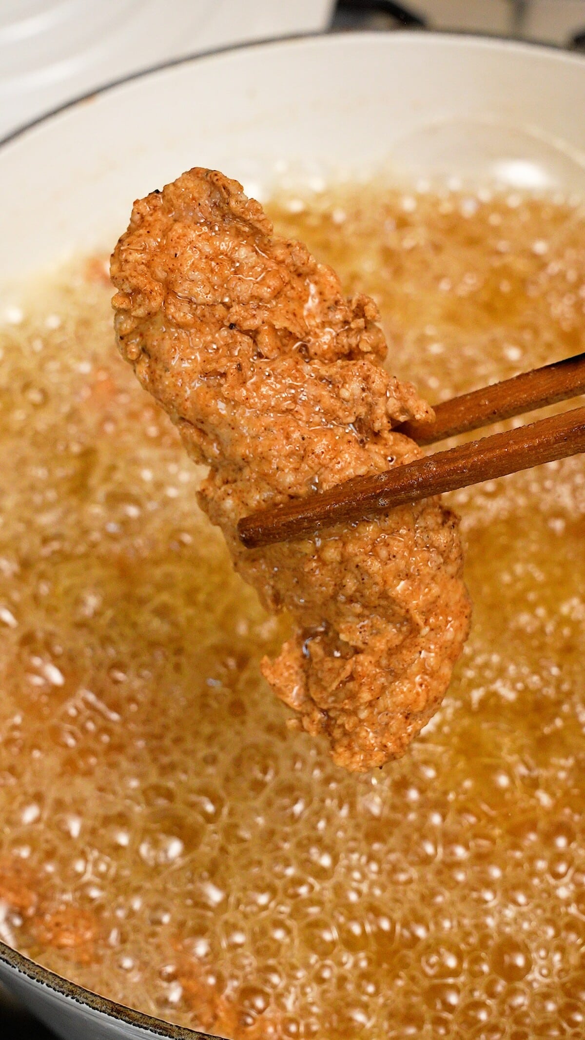 A chicken tender being held over frying oil.