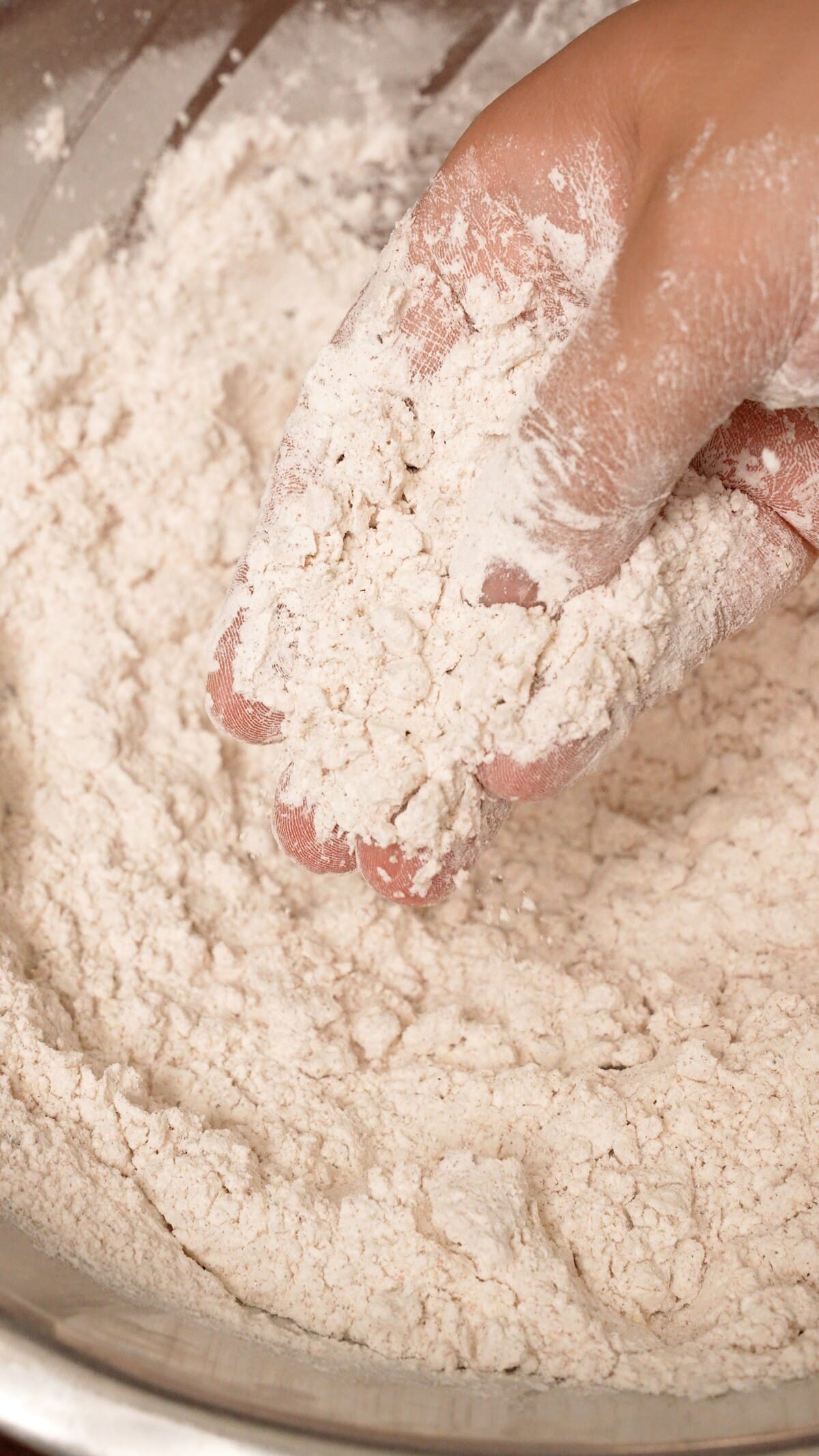 A hand creating craggily bits in the dry batter in a bowl.