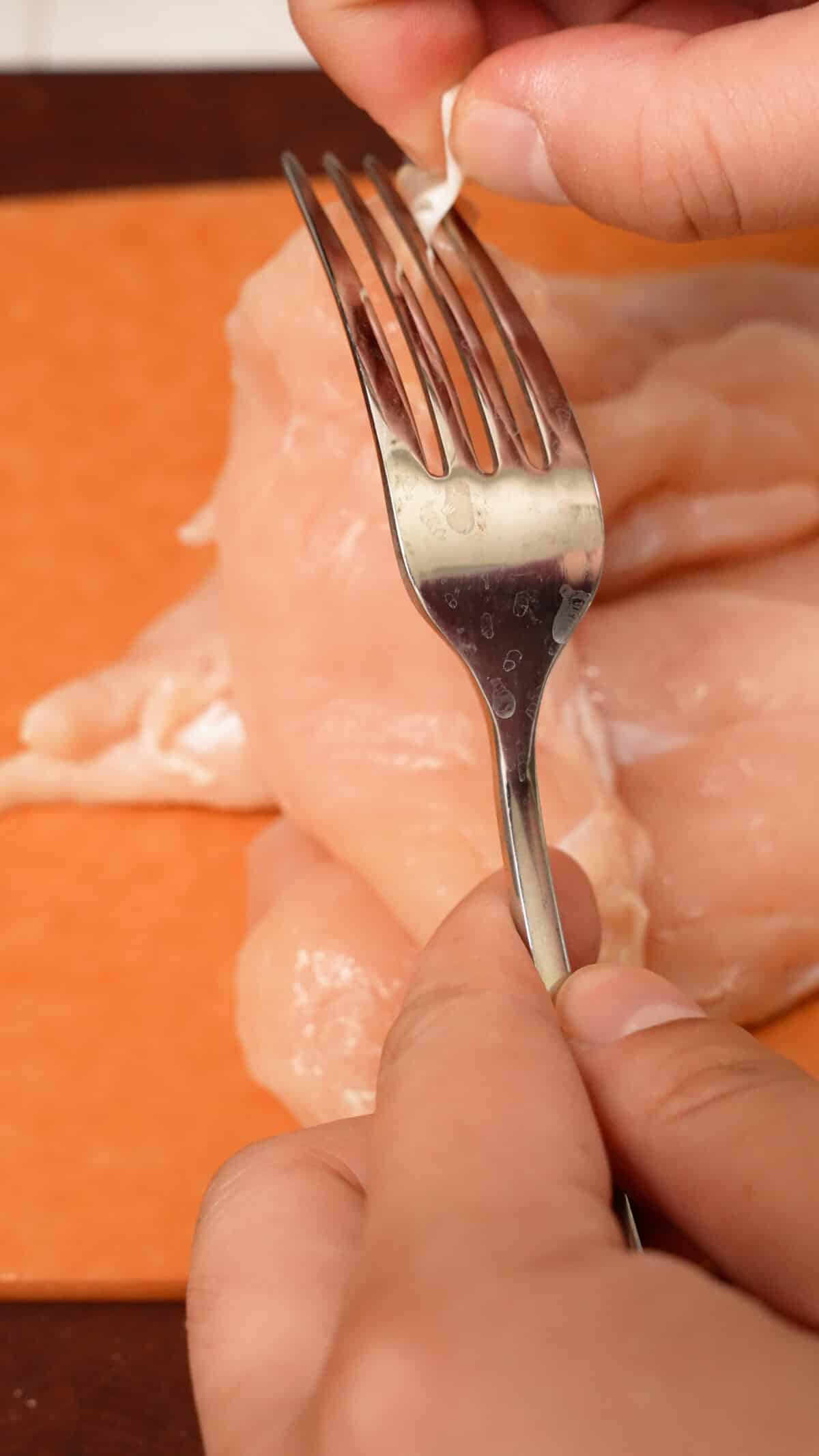 Removing tendon from a chicken tender with a fork.